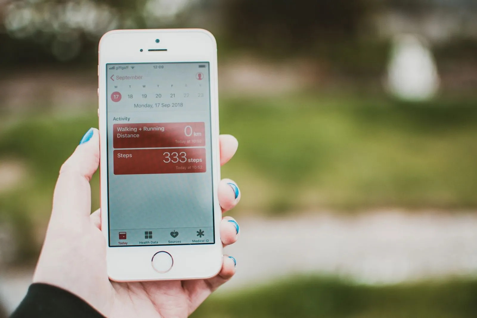 A hand holding a phone outdoors, showing a day's walking, running distance and step count.