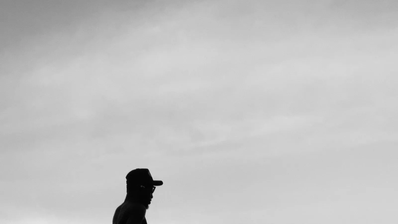 A black and white silhouette of a runner in a cap against a pale, overcast sky.